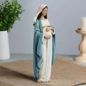 Angled side close-up of the 9.5-Inch Pregnant Virgin Mary Statue on a burlap mat with a white vase and candle holder in the background Wholesale 9.5-Inch Hand-Painted Resin Expectant Mother Mary Pregnant Statue (Our Lady of Sweet Waiting)